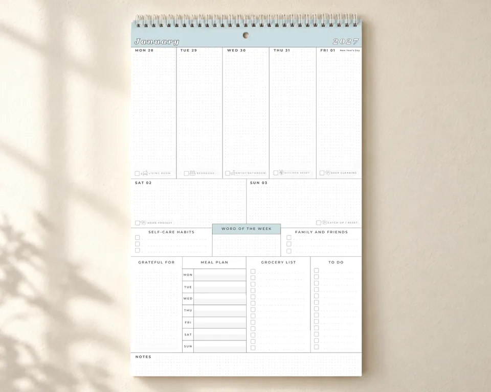 The Organized Mom Collective weekly wall calendar hanging on a wall in soft daylight, with a column for each day and sections for meals, groceries and to-dos.