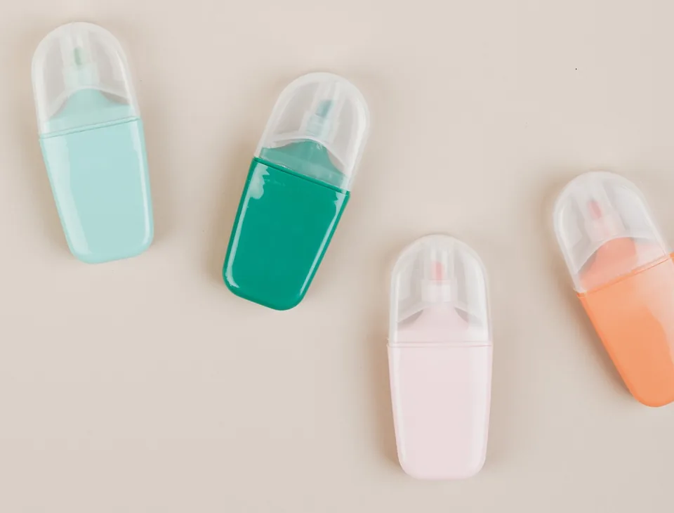Tight crop of mint, green, pale pink and peach highlighters with clear caps on a beige surface.